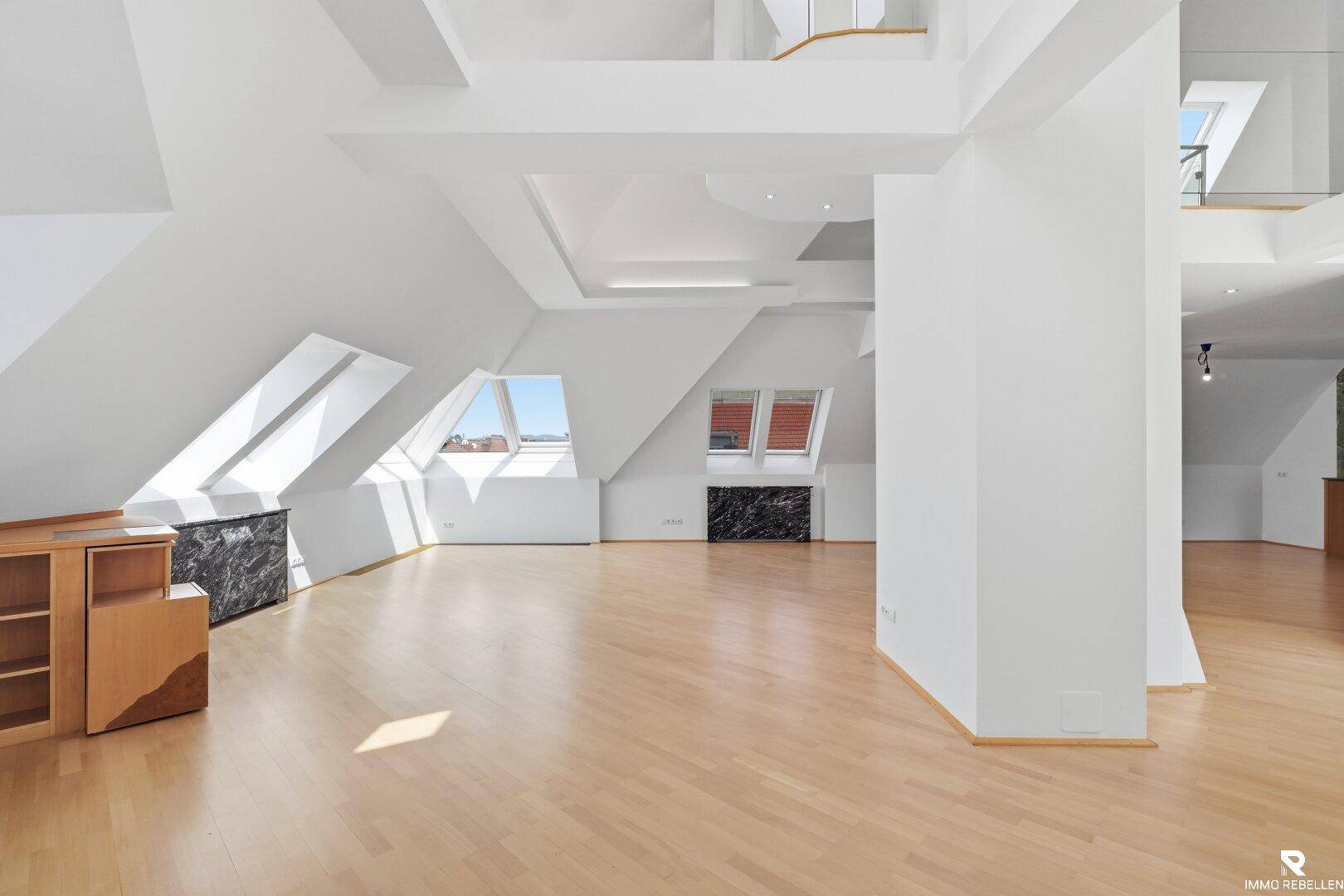 Weitläufiger Wohnbereich im Dachgeschoss mit Holzboden, hohen Decken und mehreren Dachfenstern.