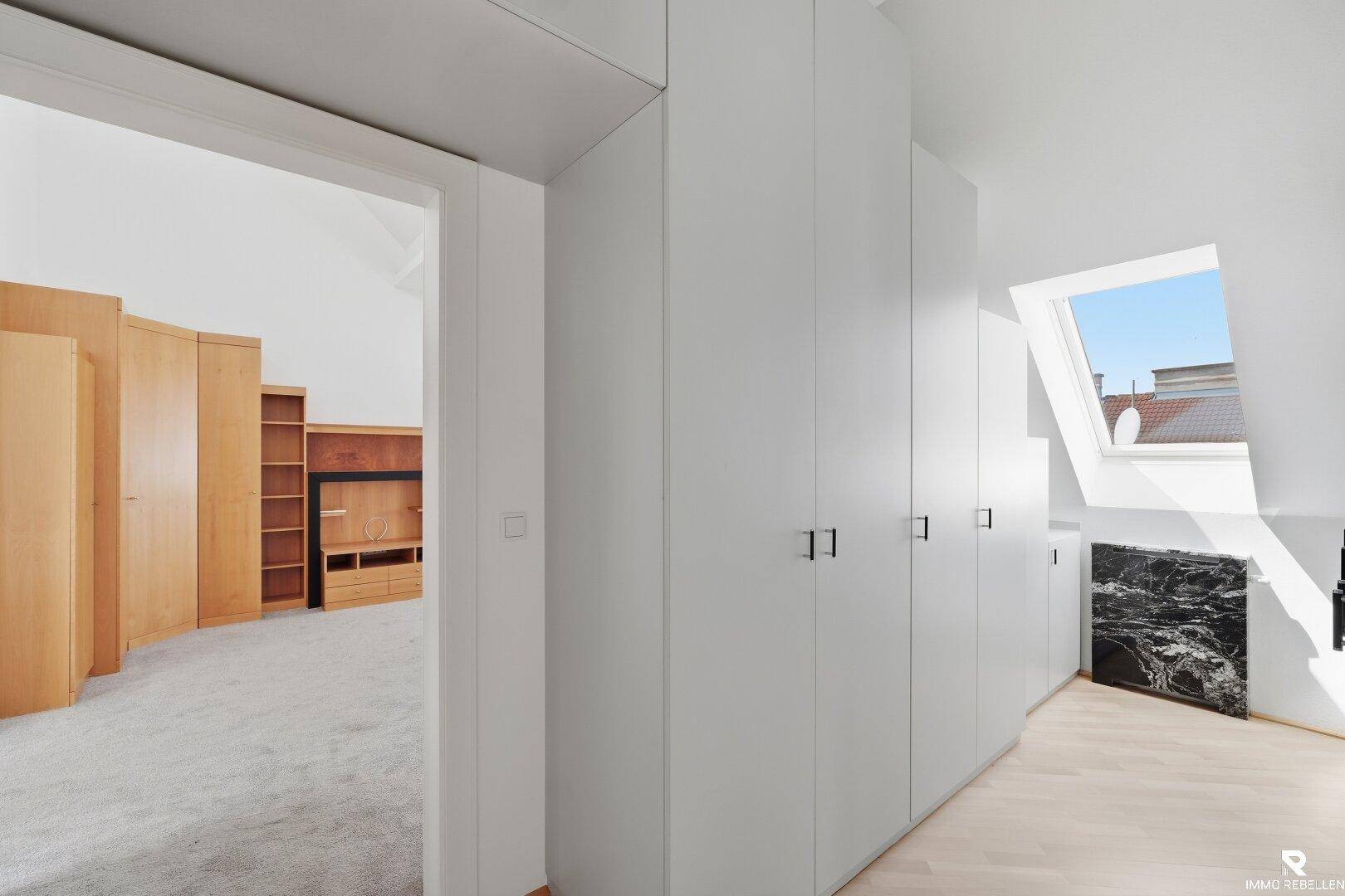 Heller Flur mit Einbauschränken, Holzboden und Dachfenster, führt zu einem weiteren Raum.
