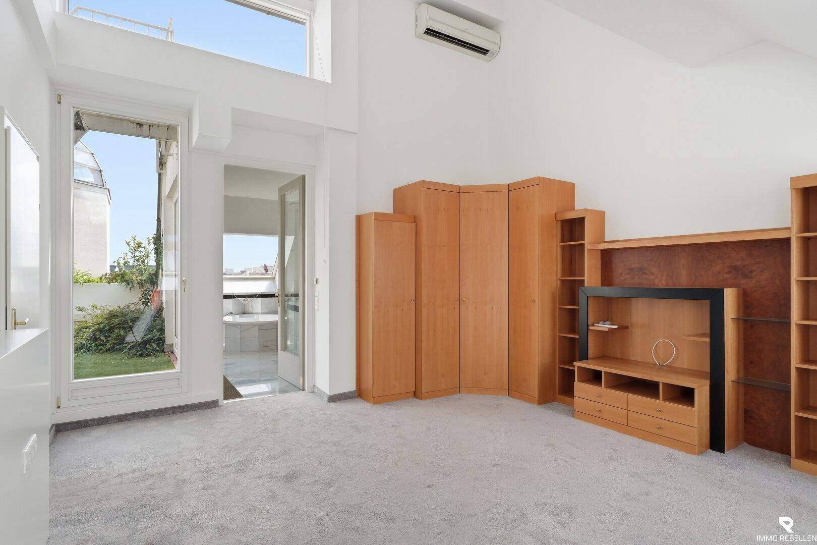 Geräumiges Wohnzimmer mit Teppichboden, Holzmöbeln und Zugang zu einem Außenbereich.