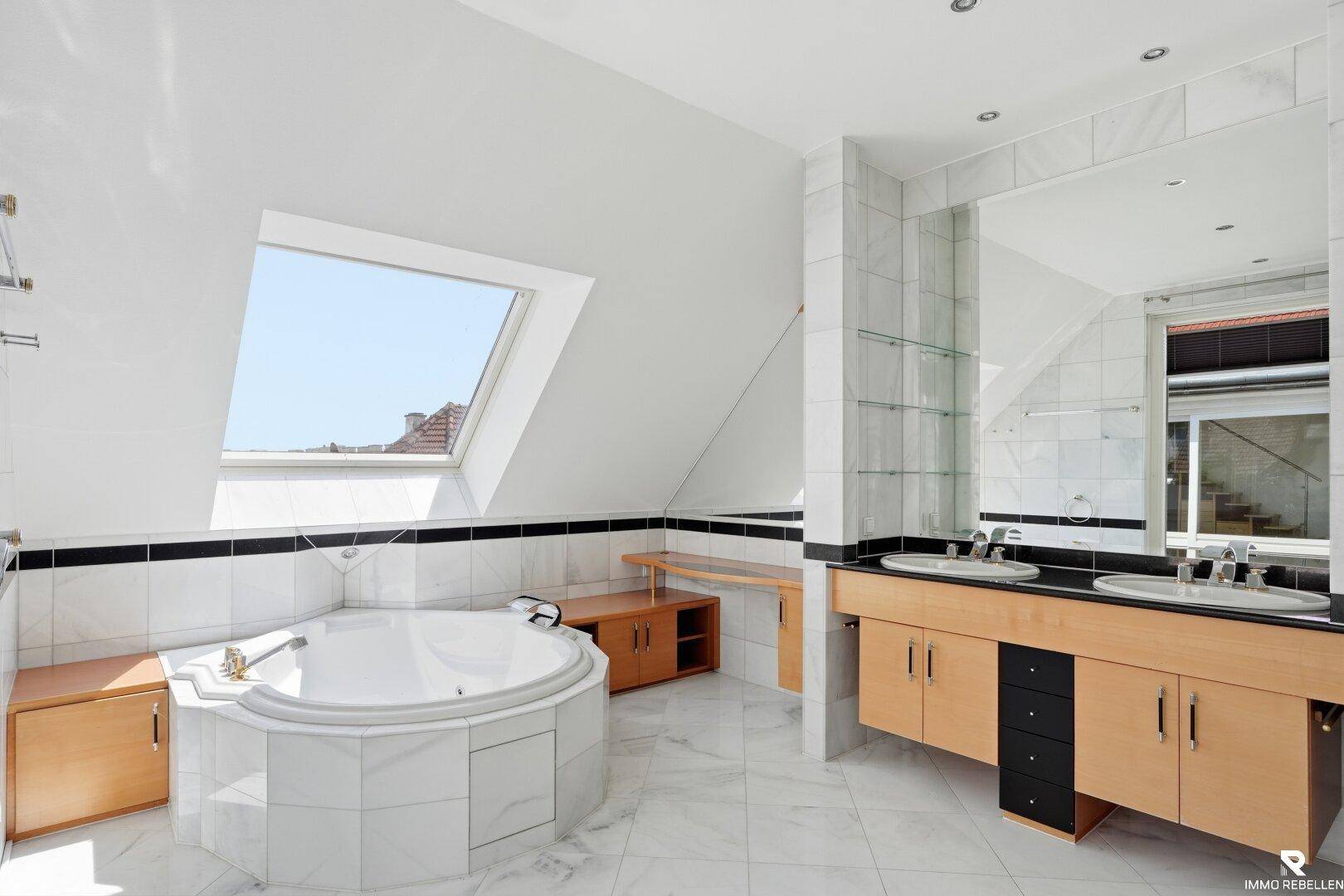 Großes Badezimmer im Dachgeschoss mit Eckbadewanne, Doppelwaschbecken und Dachfenster.