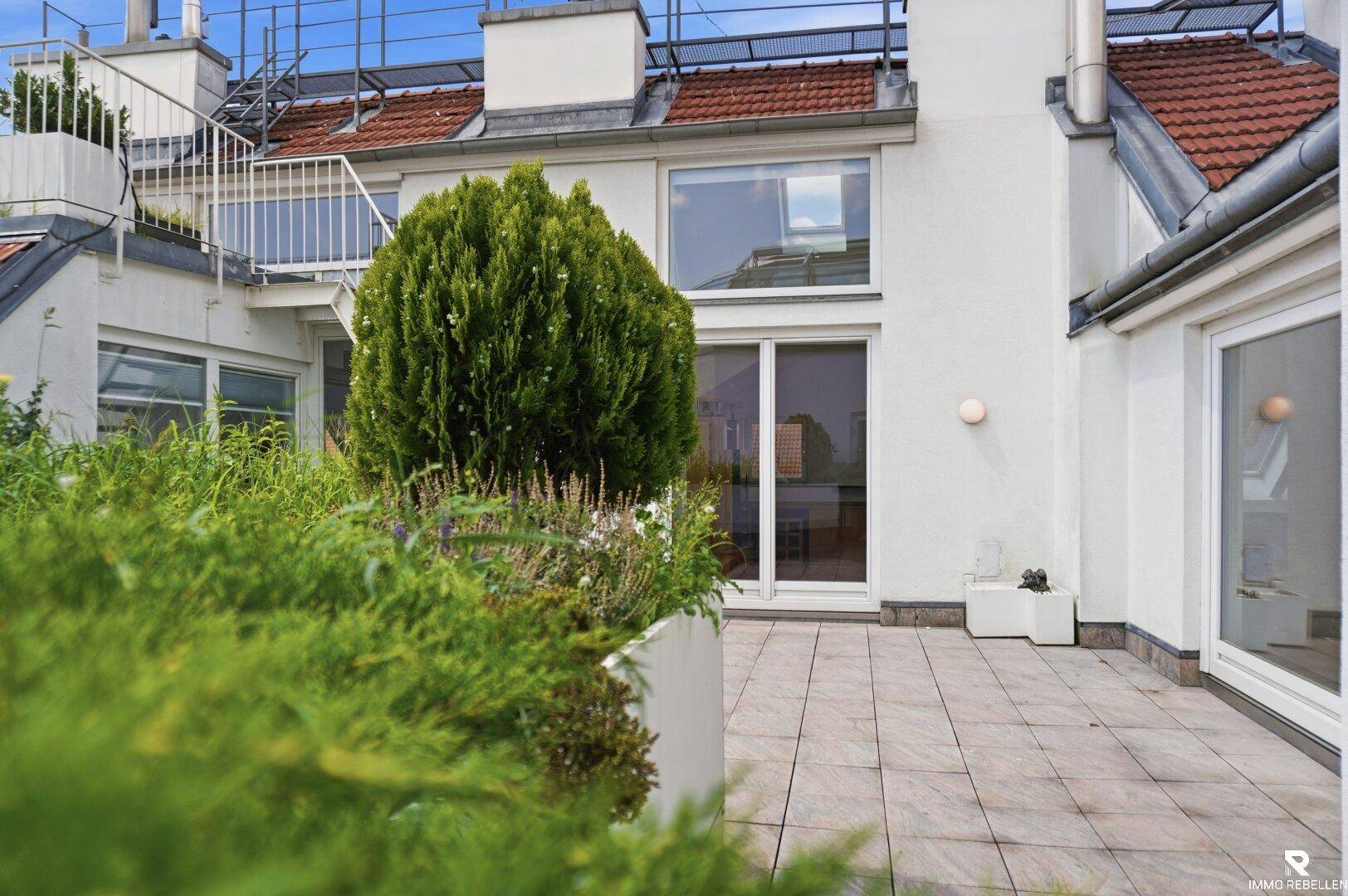 Geräumige Dachterrasse mit Fliesenboden, Pflanzenbeeten und Blick auf die Umgebung.