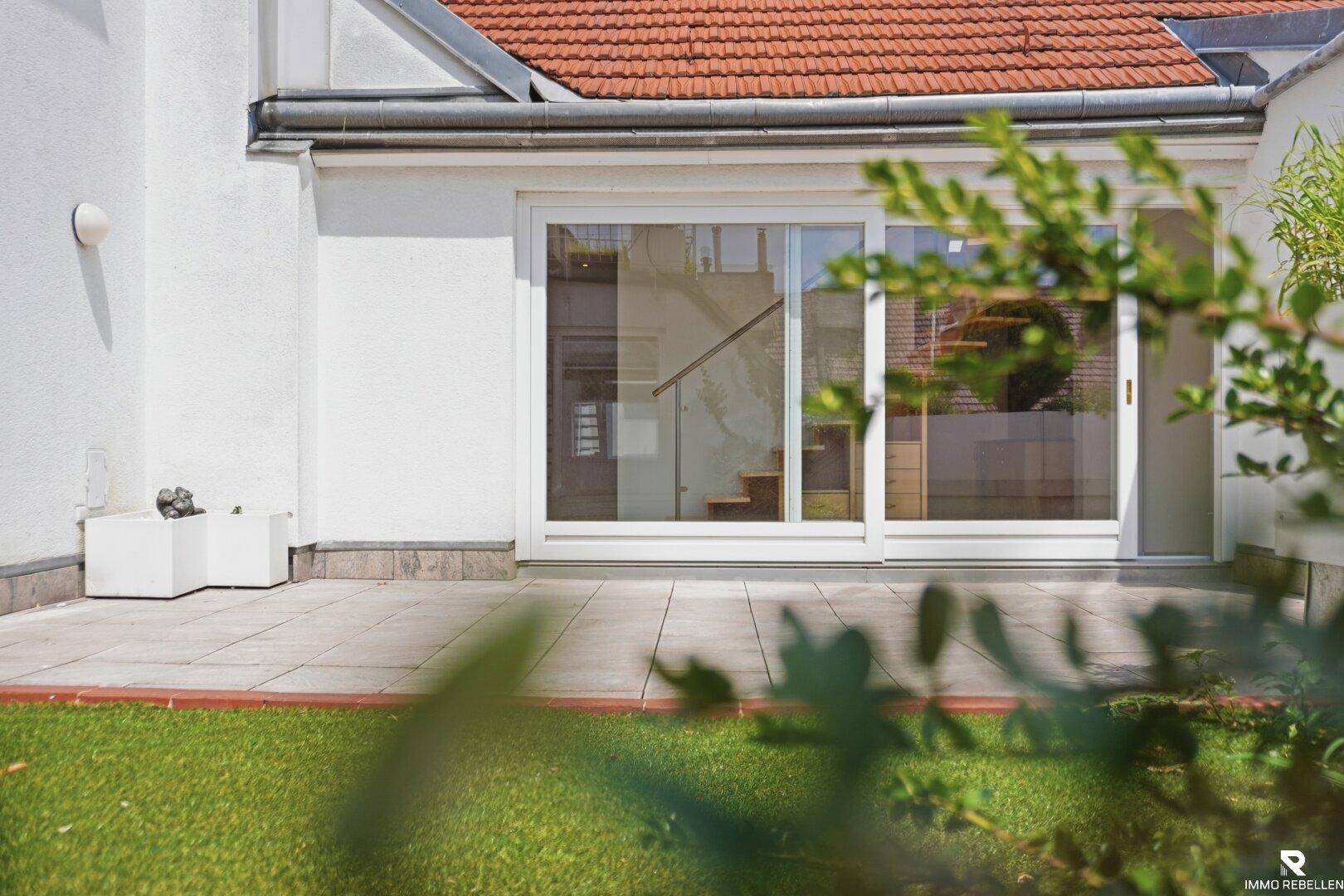 Kleiner Rasenbereich vor einer weißen Fassade mit Schiebetüren und Blick ins Innere.