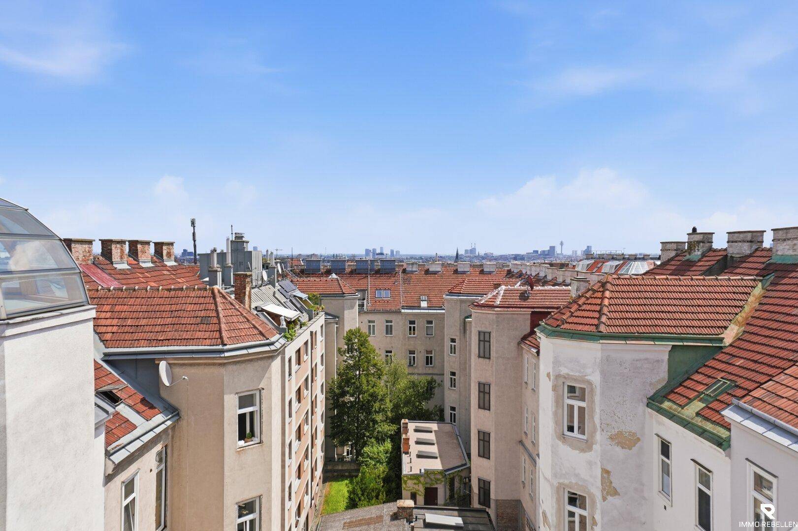 Weitläufiger Blick über die Dächer der Stadt mit historischer Architektur und blauem Himmel.