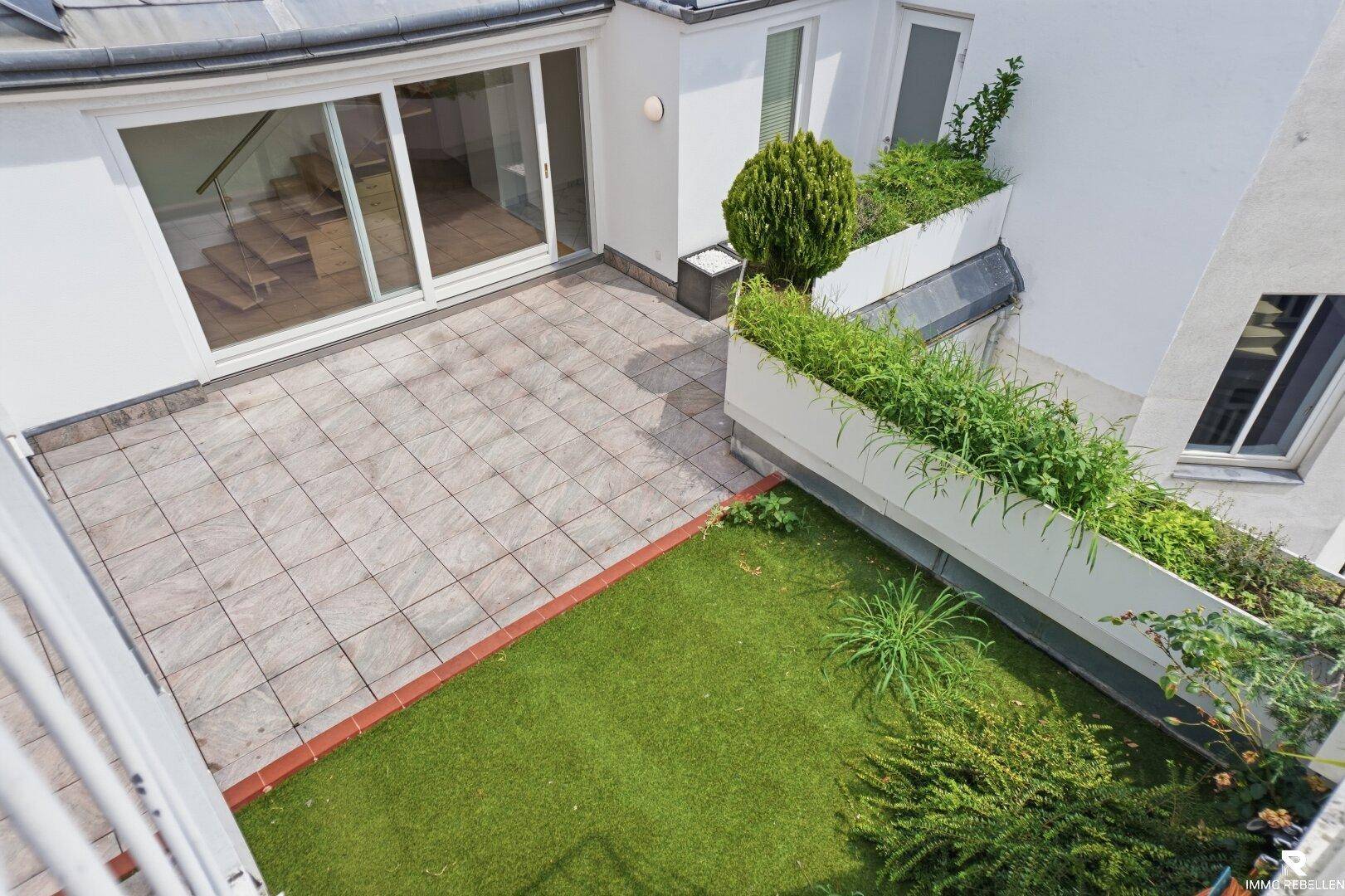 Dachterrasse mit Fliesenboden, Kunstrasenfläche und begrünten Pflanzbeeten.
