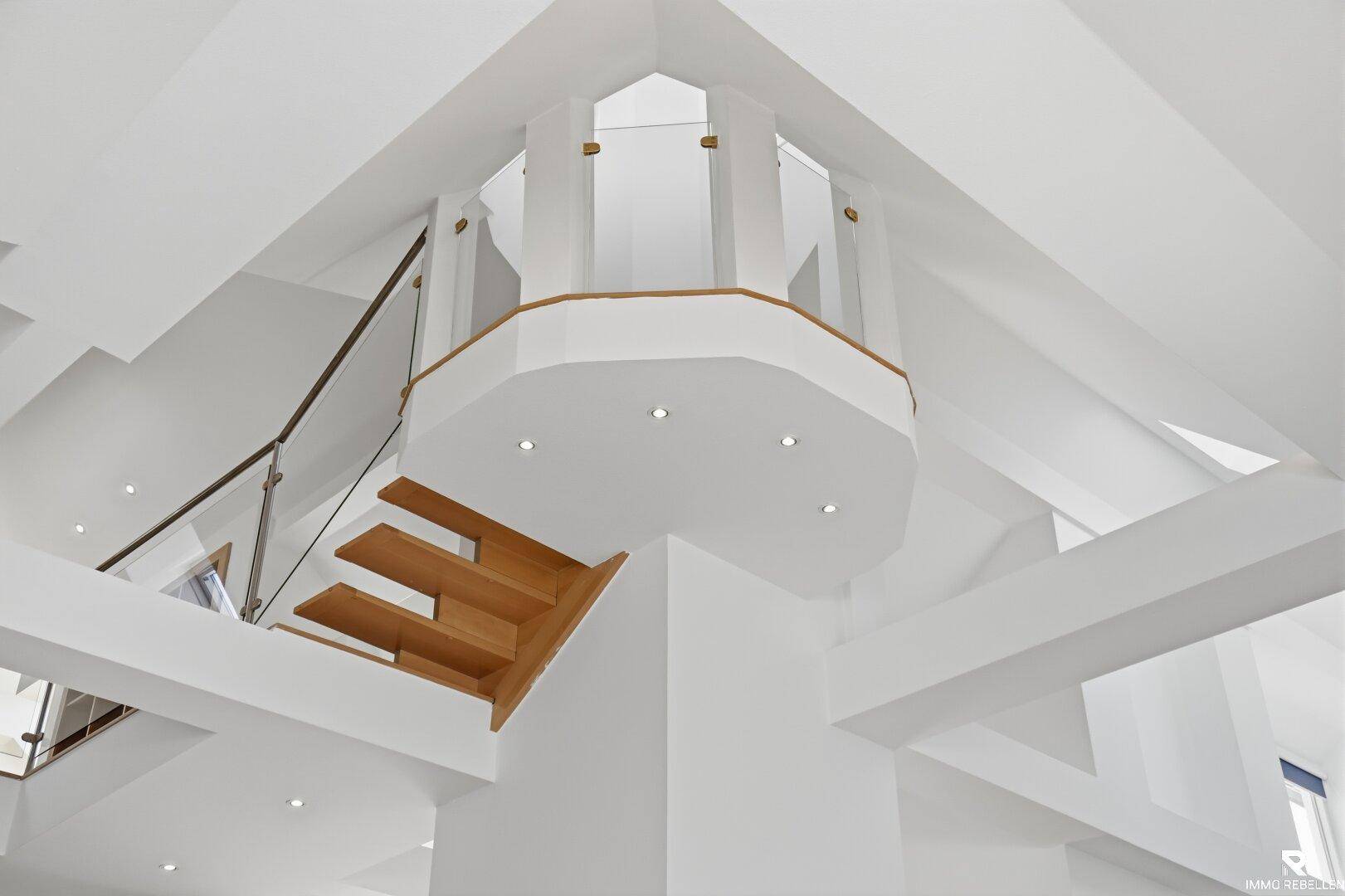 Architektonisches Detail einer modernen Holztreppe mit Glasgeländer und hohen Decken.