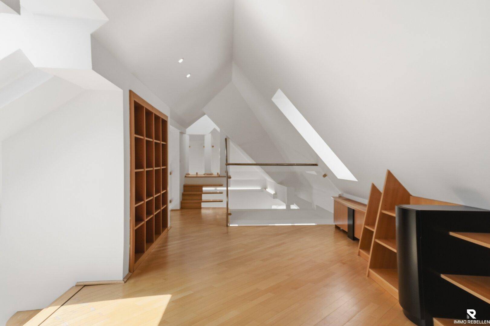 Offener Dachbodenbereich mit Holzboden, Regalen und Blick auf die moderne Treppe.