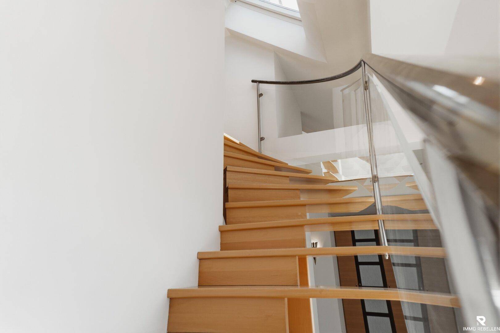 Elegante Holztreppe mit geschwungenem Glasgeländer und Metallhandlauf.