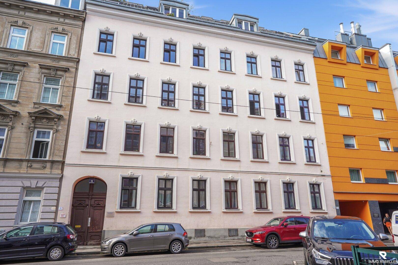 Klassische Fassade eines Mehrfamilienhauses mit vielen Fenstern und geparkten Autos davor.