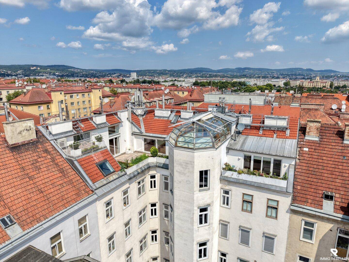 Dachlandschaft der Stadt mit roten Ziegeldächern und einem markanten Glaskuppelgebäude.