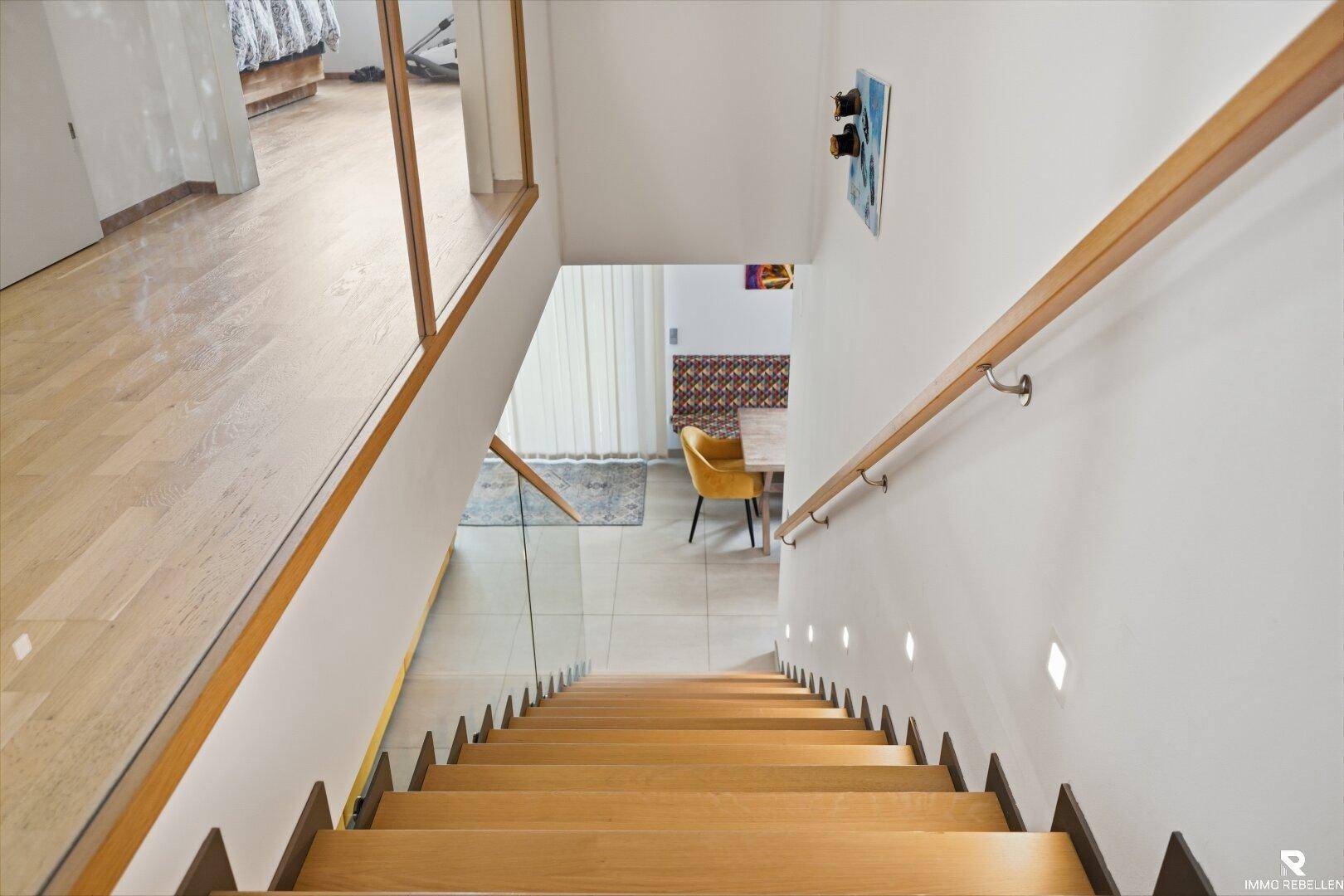 Moderne Holztreppe mit Glasgeländer und indirekter Beleuchtung führt ins Erdgeschoss.