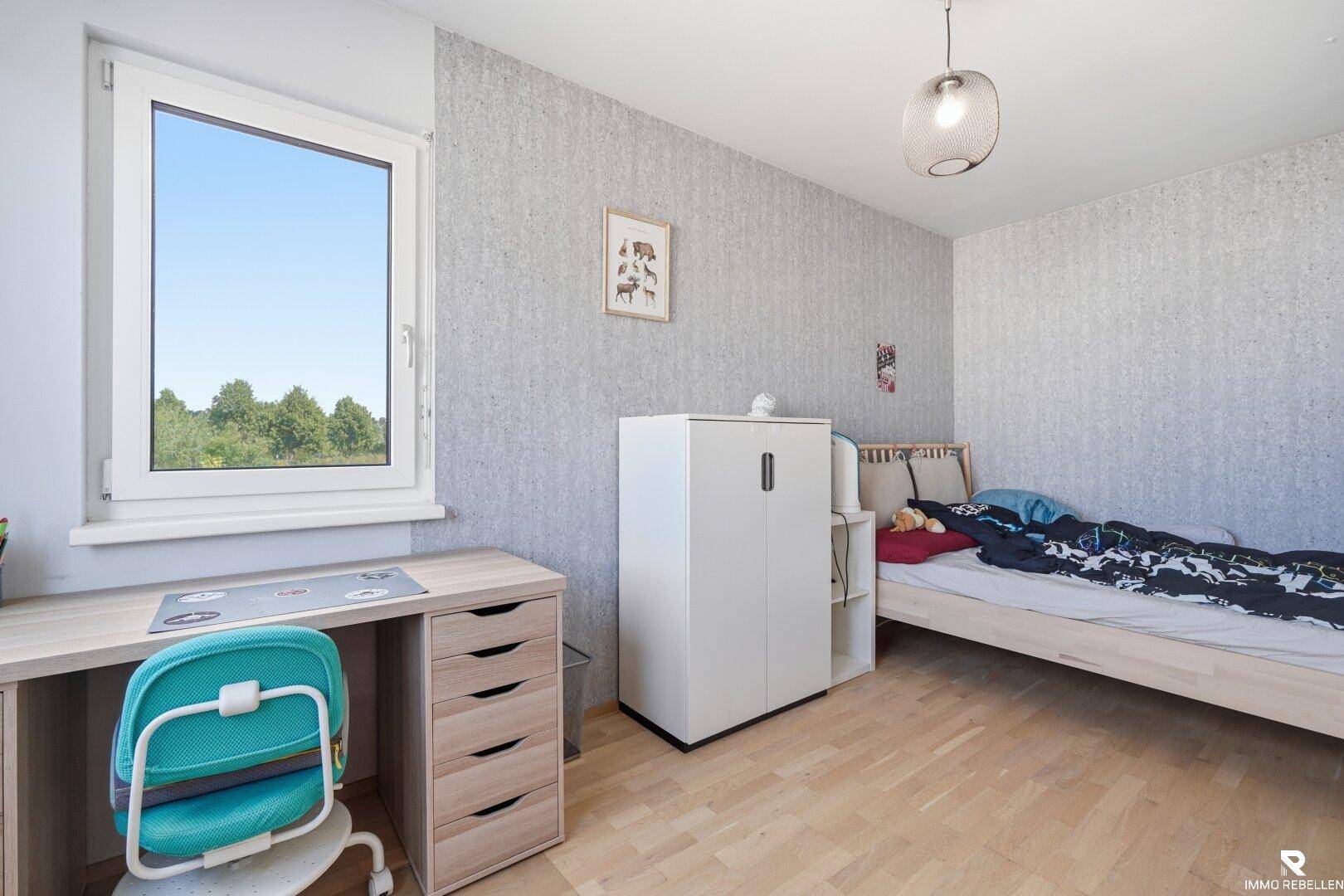 Kinderzimmer mit Bett, Schreibtisch und gemusterter Tapete, hell und freundlich.