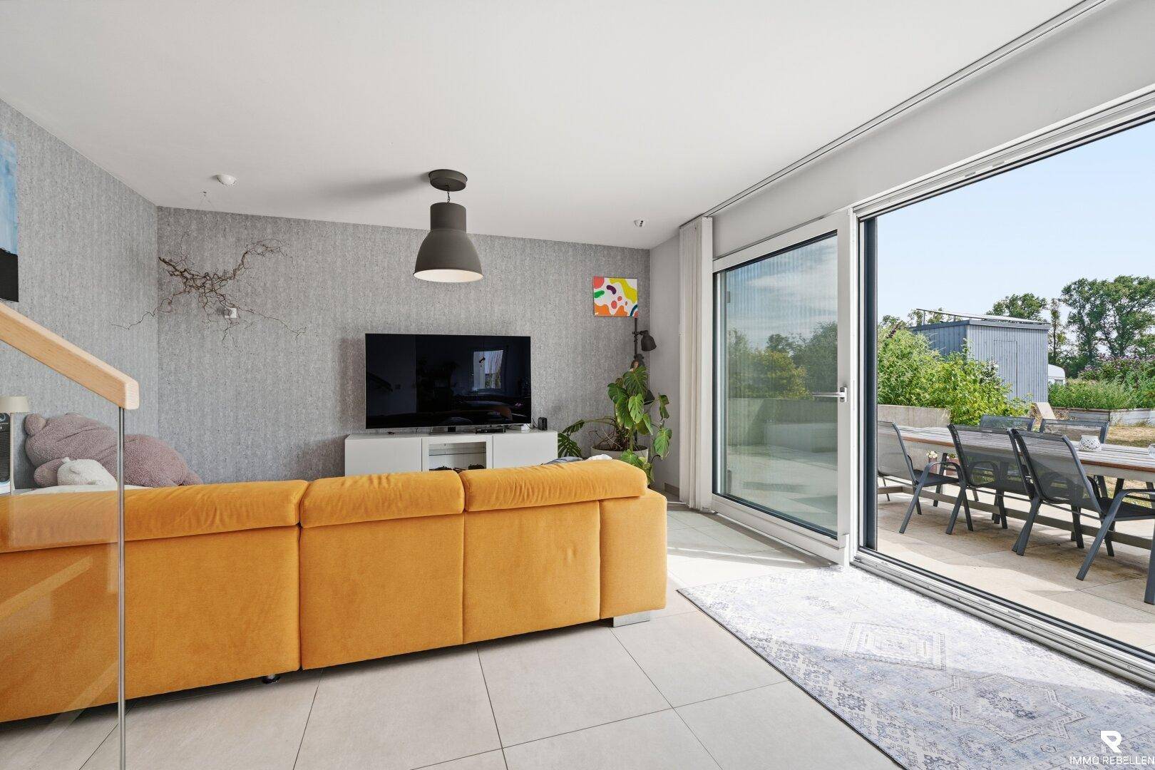 Modernes Wohnzimmer mit gelbem Sofa, Fernseher und Schiebetür zur Dachterrasse.