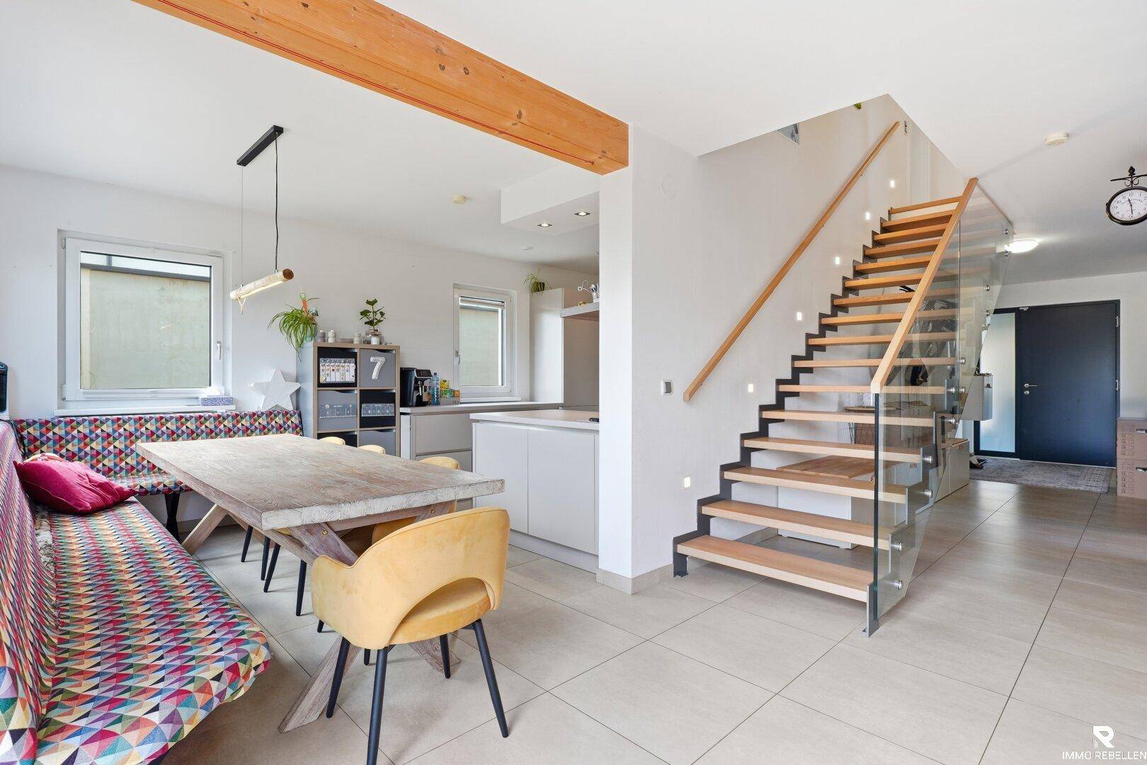 Offener Essbereich mit Holztisch, Sitzbank und moderner Treppe zum Obergeschoss.