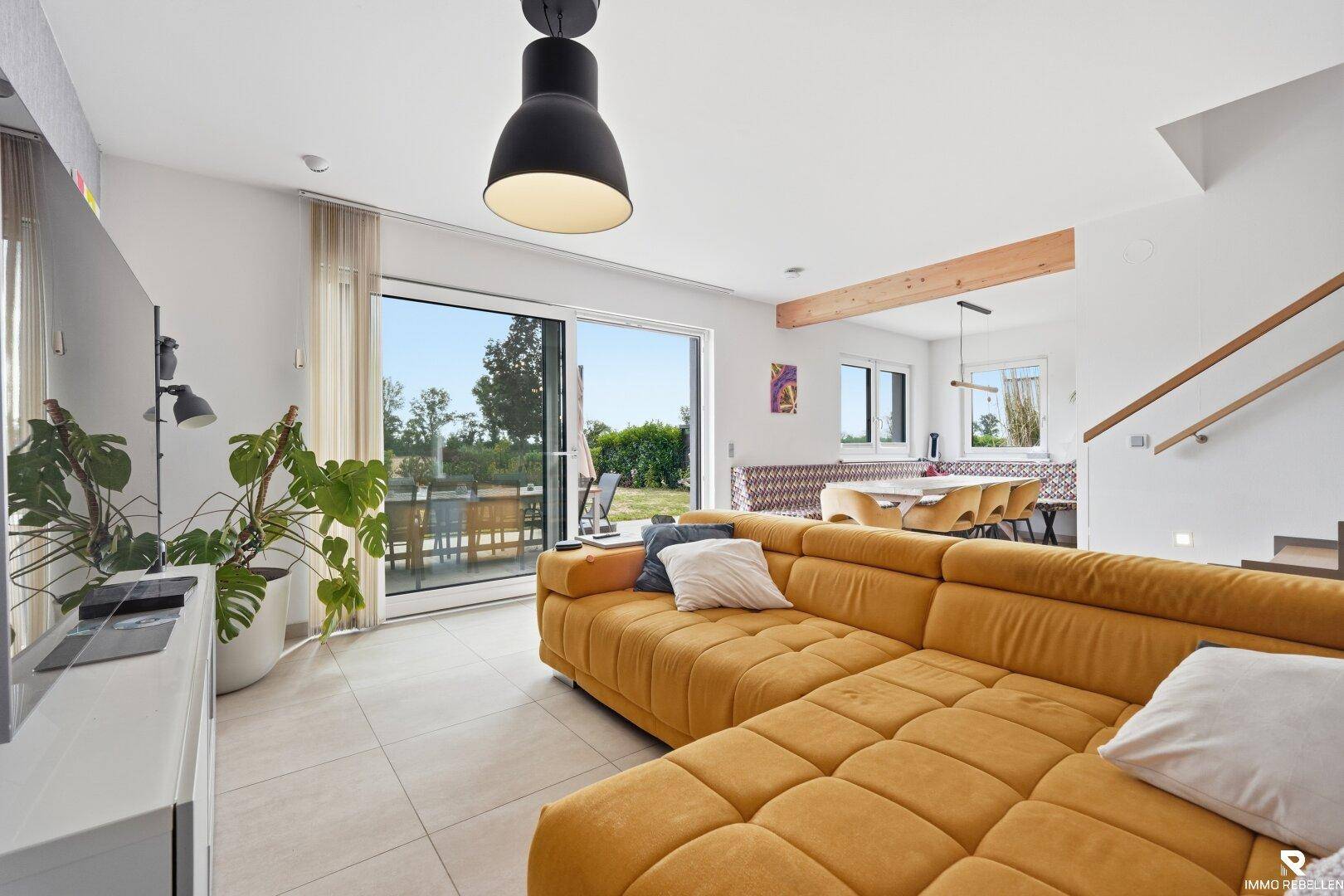 Gemütliches Wohnzimmer mit großem Ecksofa, Fliesenboden und Zugang zur Terrasse.
