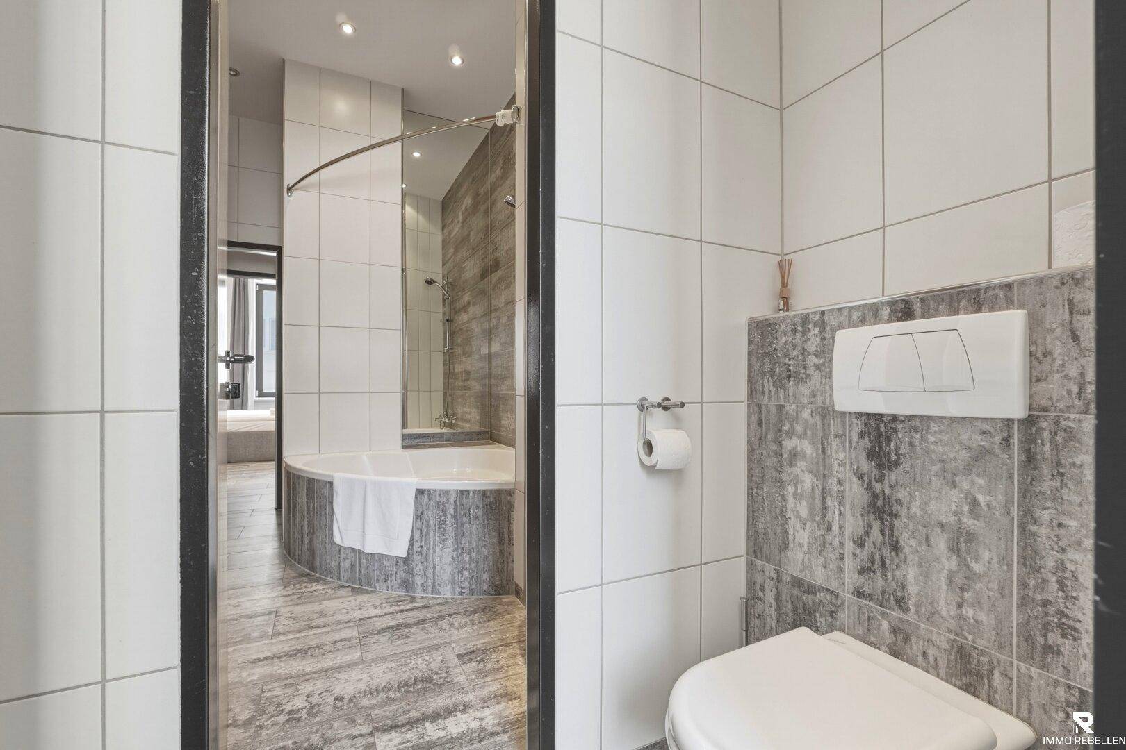 Badezimmer mit Toilette und Blick auf eine runde Badewanne, modern gefliest.