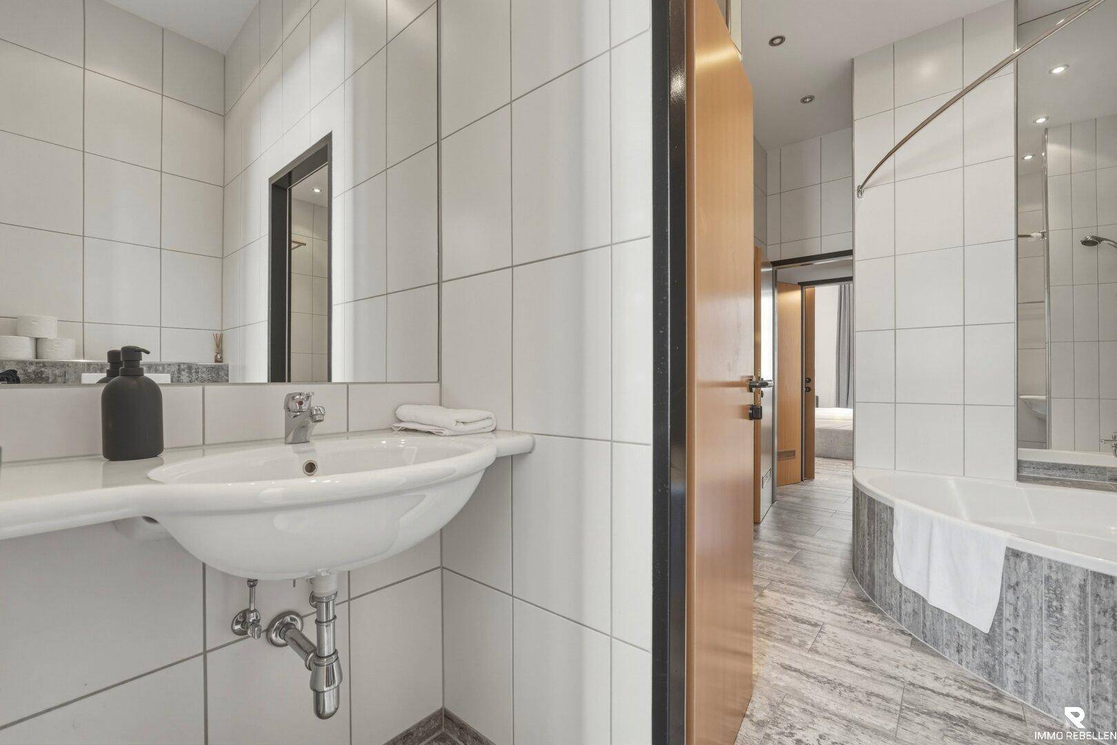 Helles Badezimmer mit Waschbecken, Spiegel und Blick auf die Badewanne, sauber und funktional.