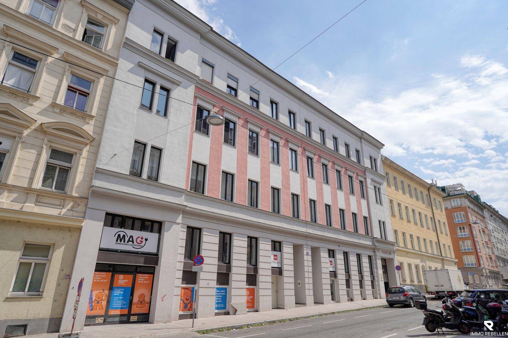 Attraktive Straßenfassade eines Mehrfamilienhauses mit Geschäften im Erdgeschoss und farbigen Akzenten.
