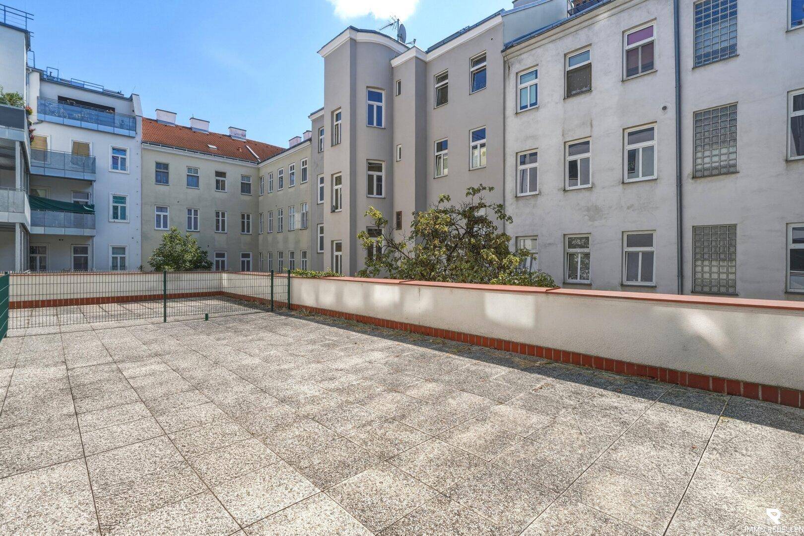 Weitläufige, leere Terrasse mit Fliesenboden und Blick auf die Architektur des Innenhofs.