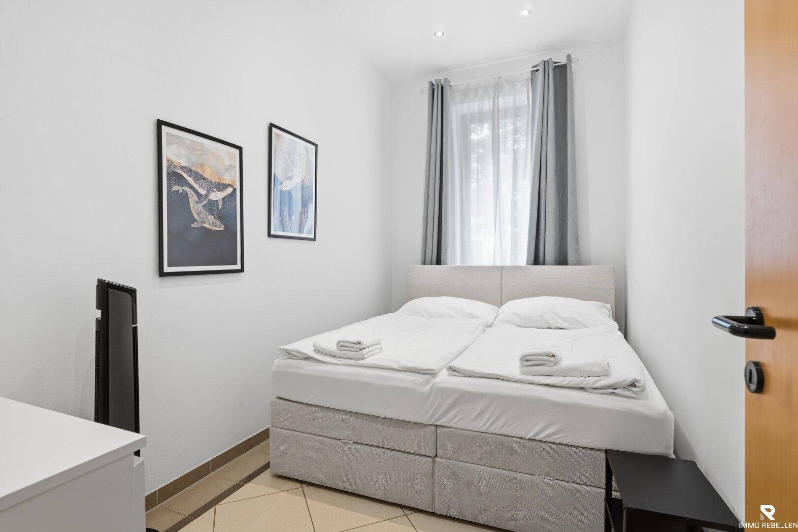 Gemütliches Schlafzimmer mit Doppelbett, kleinem Fenster und schlichter, funktionaler Einrichtung.