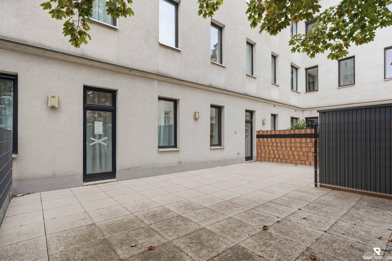 Große, geflieste Terrasse im Innenhof mit Zugang zu mehreren Türen und einem modernen Schuppen.