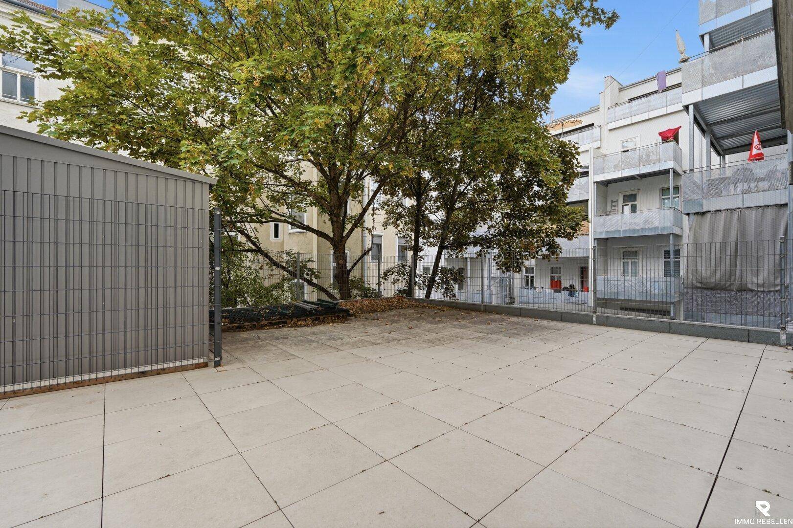 Weitläufige, geflieste Terrasse mit Blick auf umliegende Gebäude und Bäume, ideal für Entspannung.