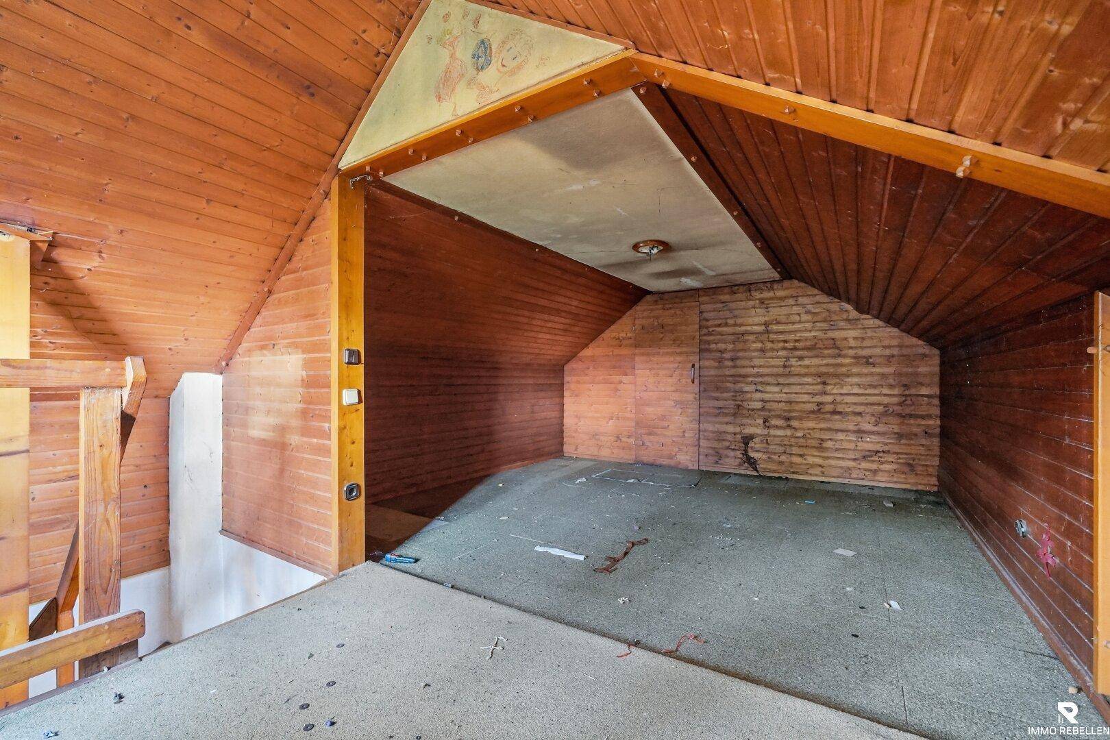 Dachgeschossraum im Originalzustand mit Holzverkleidung und schrägen Wänden, ideal als Stauraum.