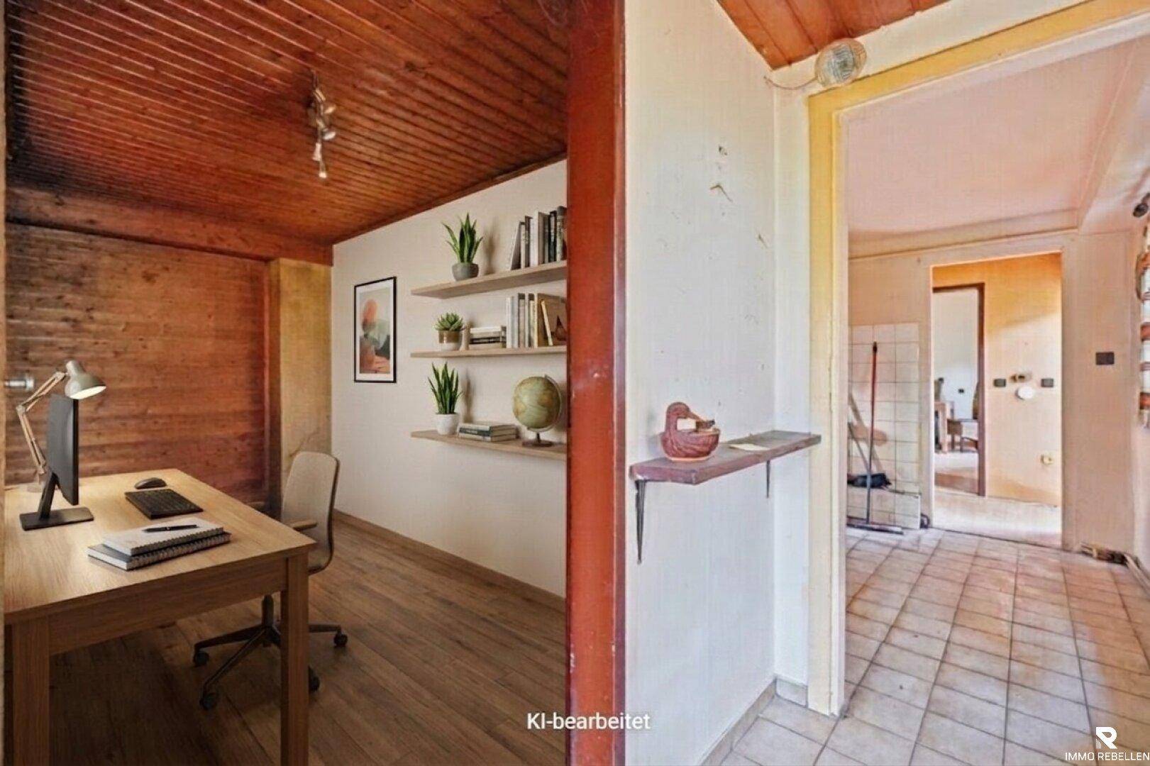 Gemütliches Büro mit Holzbalkendecke, Schreibtisch und Regalen, offen zum Flurbereich.