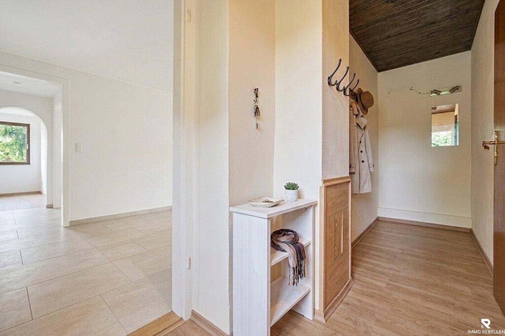 Heller Flur mit Fliesenboden, Holzelementen und Garderobe, offen zu weiteren Räumen.