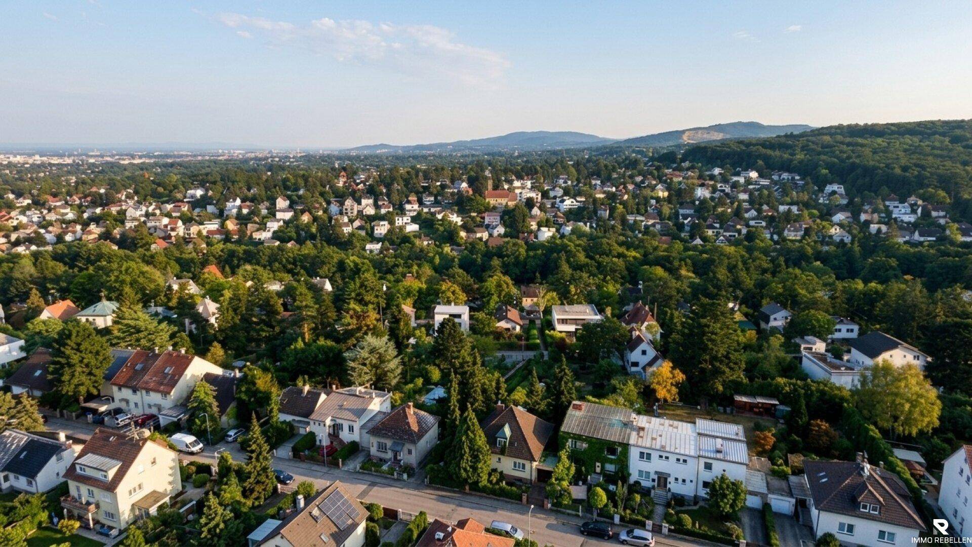 Weitläufige Wohngegend mit vielen Häusern und üppiger Vegetation, umgeben von bewaldeten Hügeln.