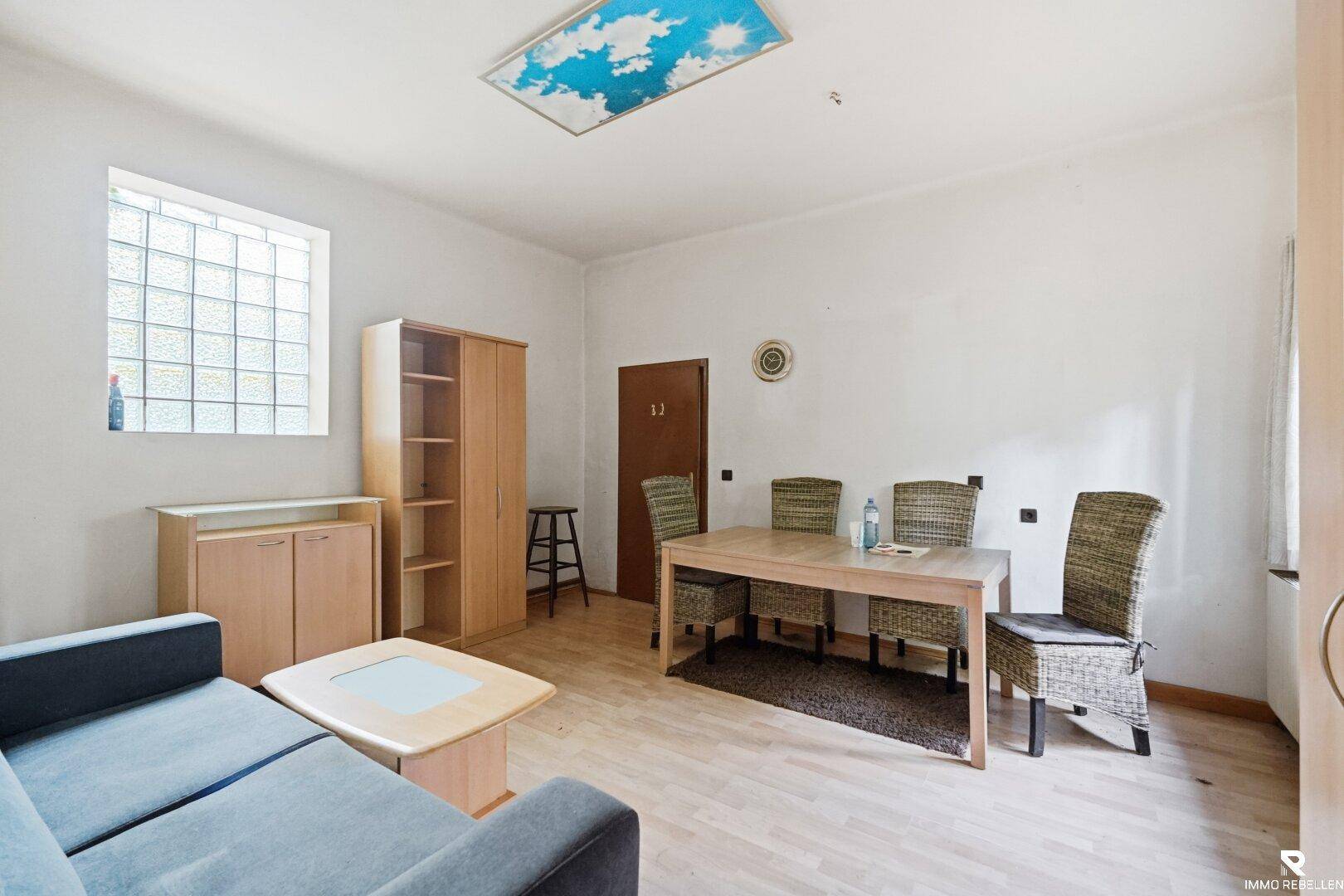Heller Wohn- und Essbereich mit Esstisch, Sofa und Schrank, beleuchtet durch ein großes Fenster.