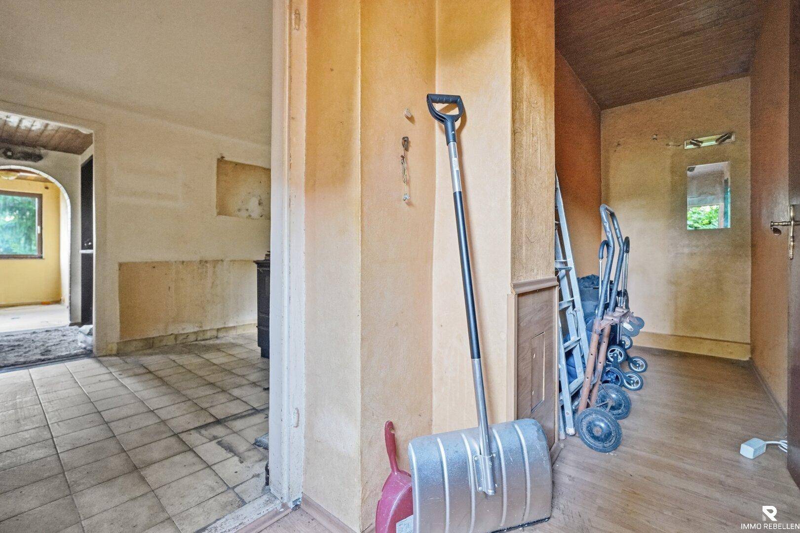 Flur im Originalzustand mit Fliesenboden und Holzelementen, benötigt Renovierung.