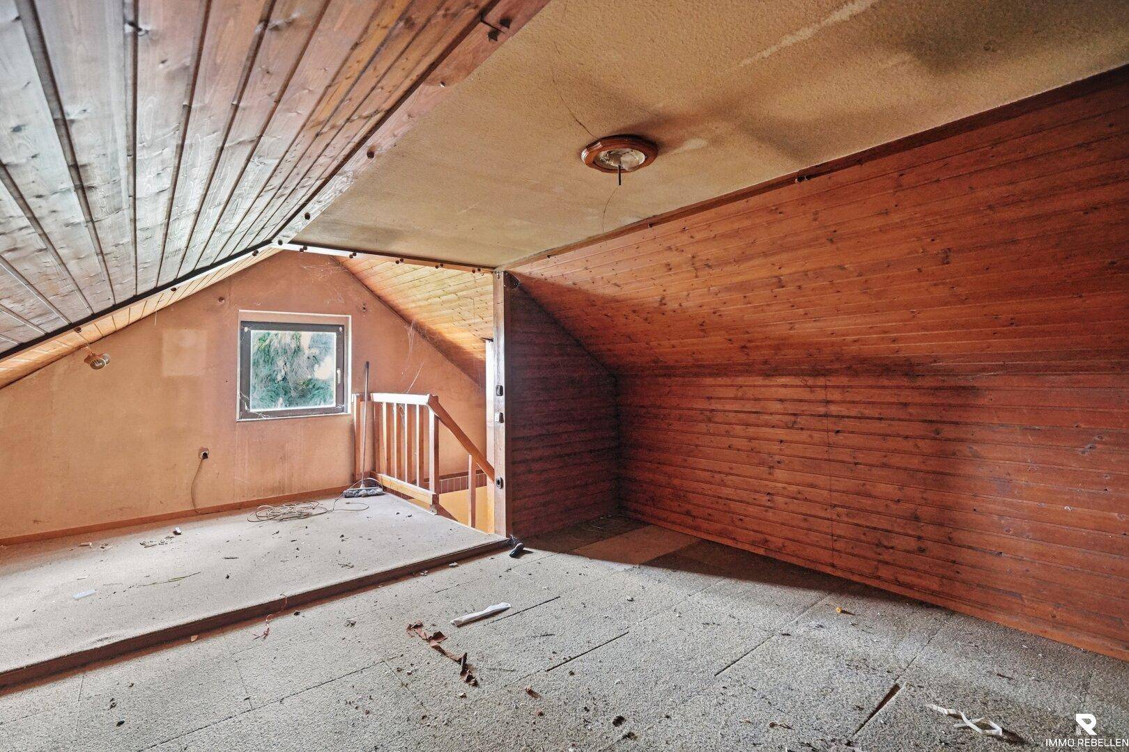 Schlafzimmer im Dachgeschoss im Originalzustand mit Holzverkleidung und schrägen Wänden.