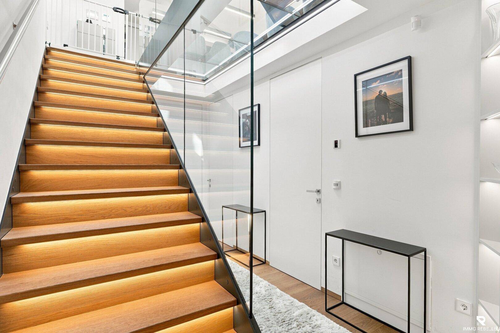 Elegante Holztreppe mit Glasgeländer und integrierter Beleuchtung in einem hellen Flur.