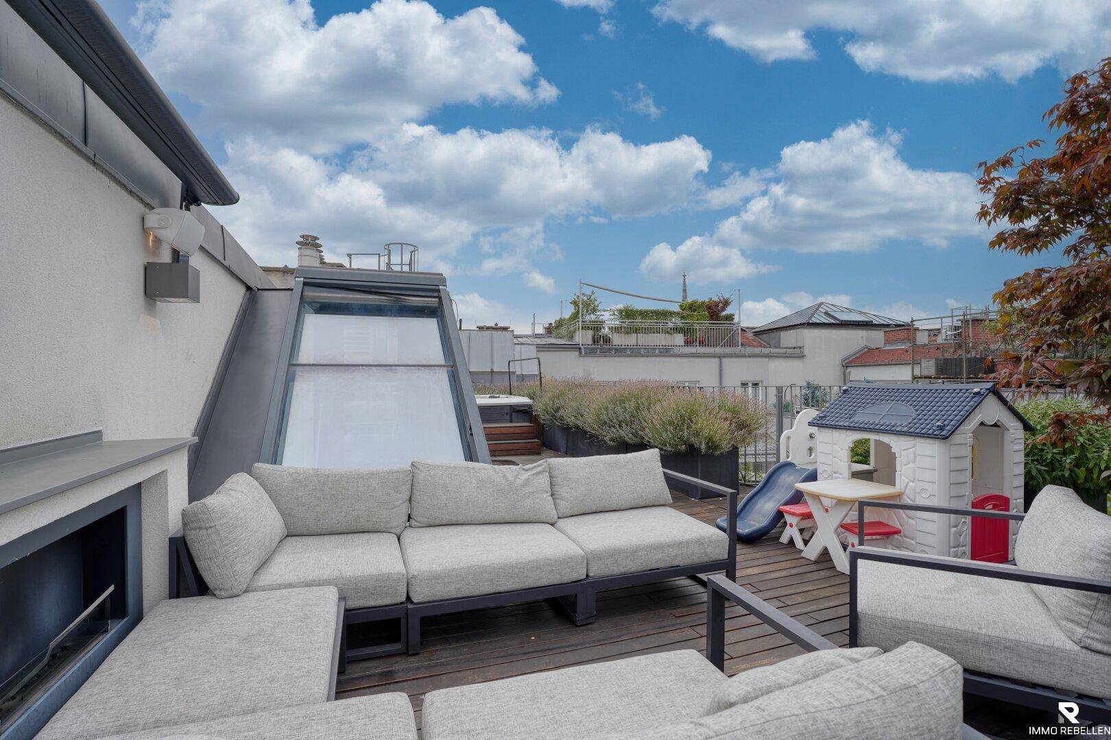 Sonniger Sitzbereich auf der Dachterrasse mit Kinderspielhaus und Blick auf die Umgebung.