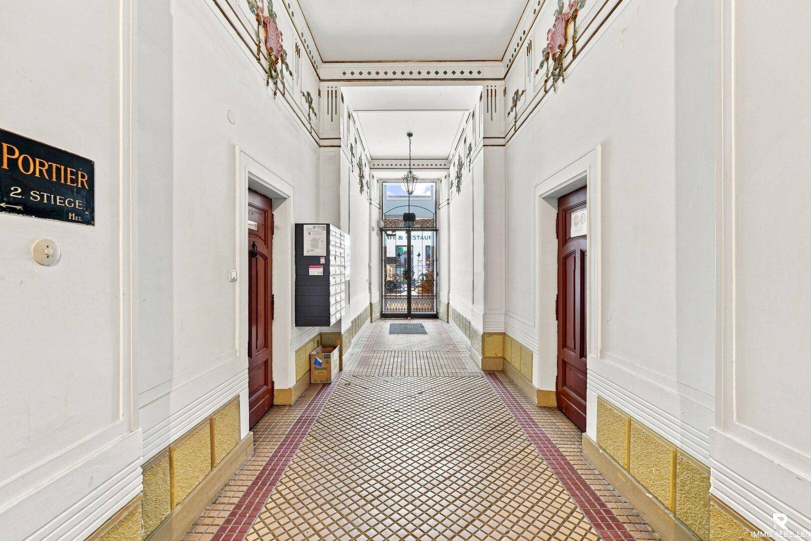 Historischer Eingangsbereich mit kunstvollen Decken- und Wandverzierungen, Fliesenboden und Holztüren.