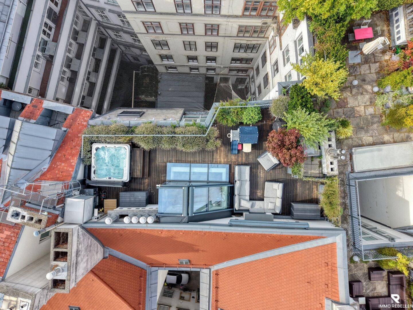 Großzügige Dachterrasse mit Whirlpool, Lounge-Möbeln und Pflanzen, umgeben von Stadtgebäuden.