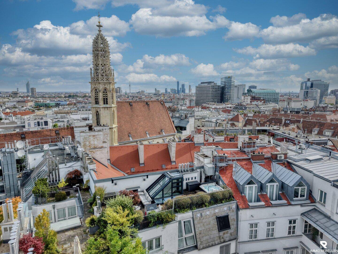 Weitläufiger Stadtblick über die Dächer mit einem historischen Kirchturm und begrünten Dachterrassen.