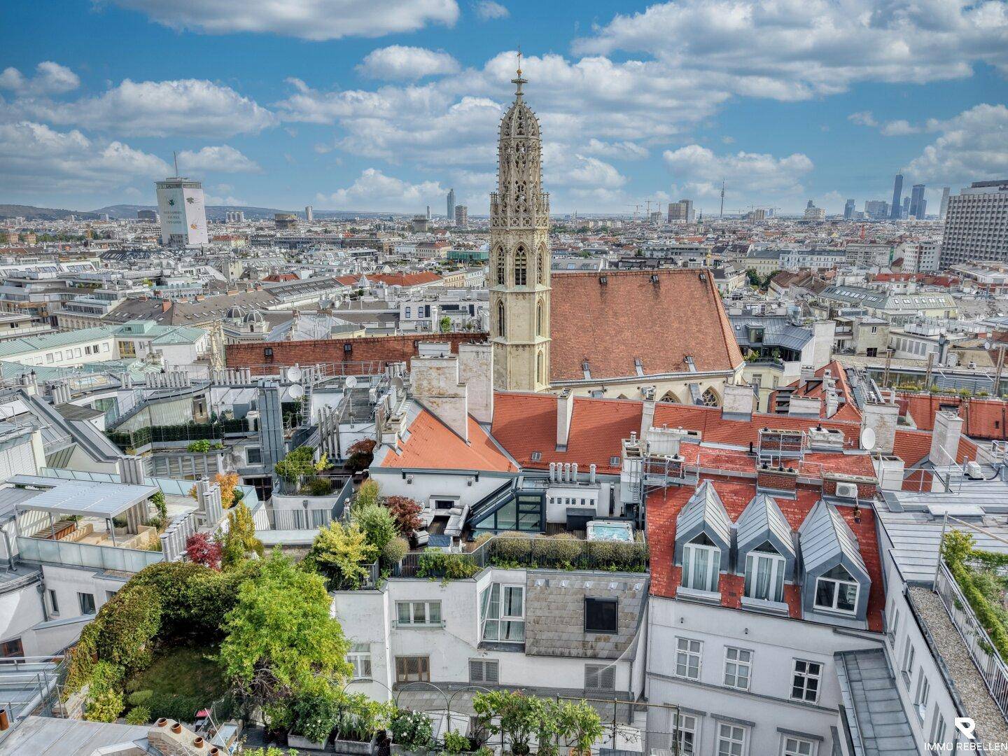 Panoramablick über die Stadt Wien mit historischer Kirche und moderner Skyline im Hintergrund.