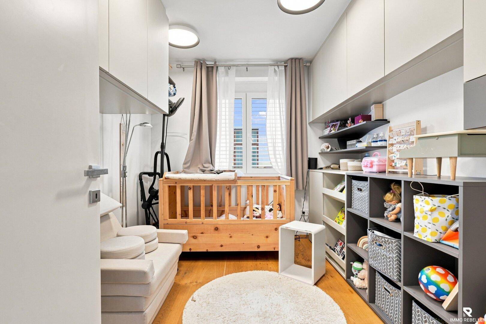 Heller Raum mit Babybett, Spielzeug und praktischen Regalen.