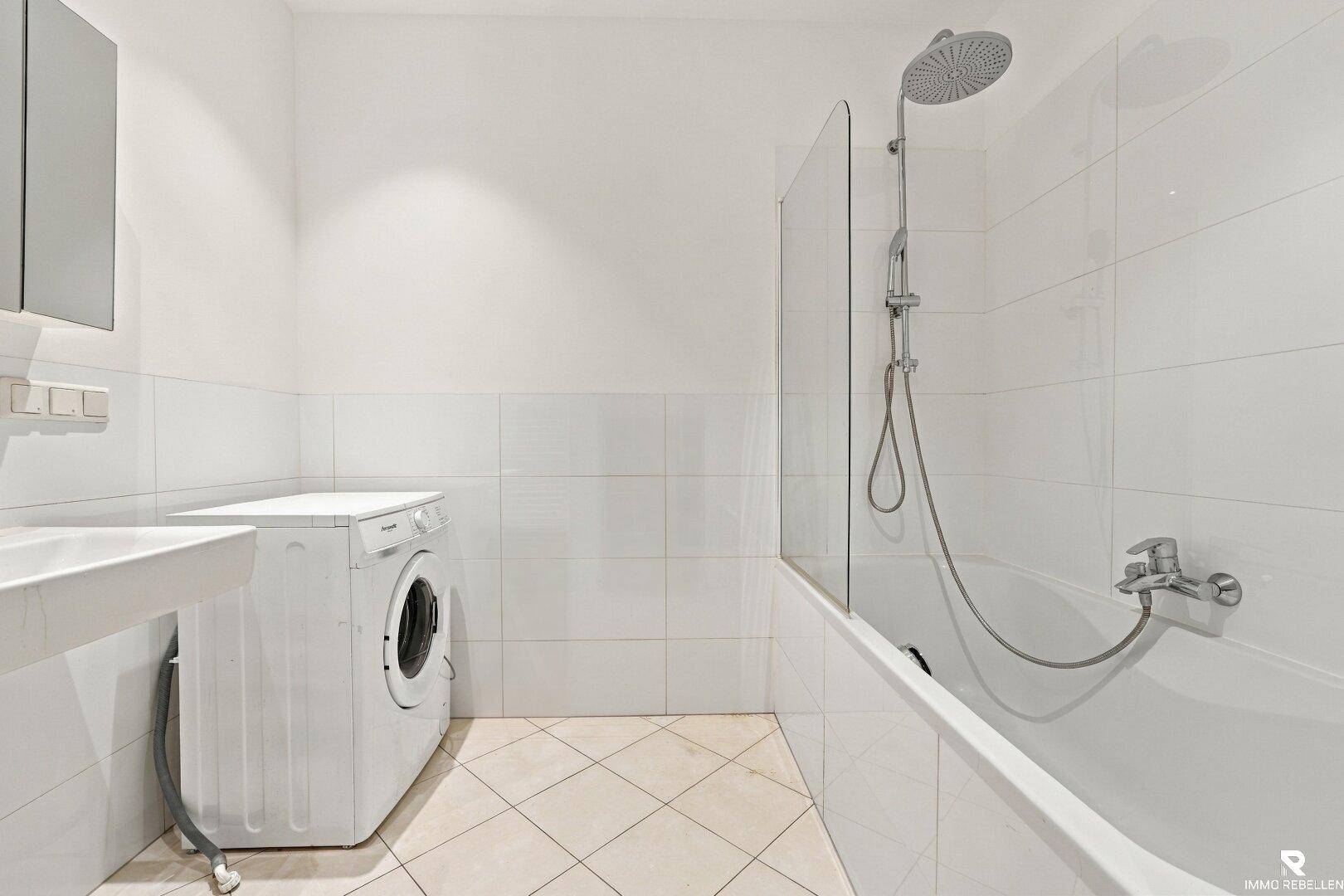 Modernes Badezimmer mit Badewanne, integrierter Dusche, Waschbecken und Waschmaschine.