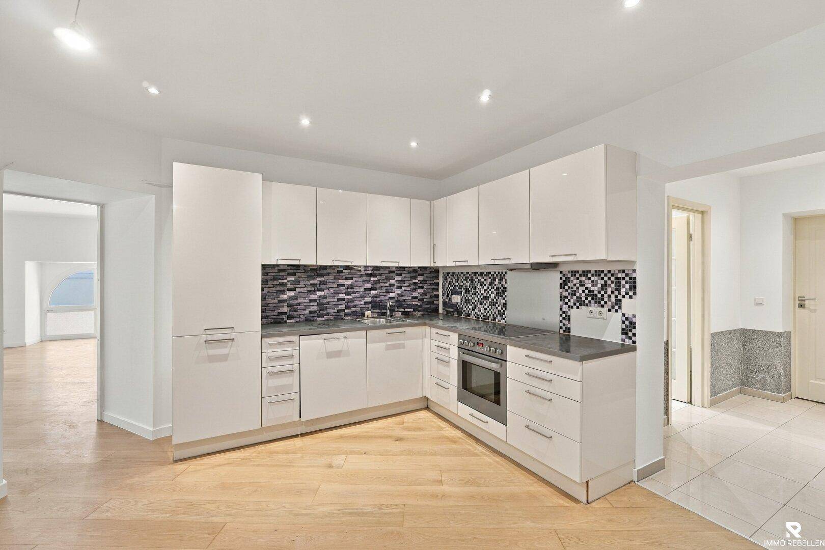 Moderne, weiße Einbauküche mit dunkler Arbeitsplatte und Mosaikfliesen als Spritzschutz.