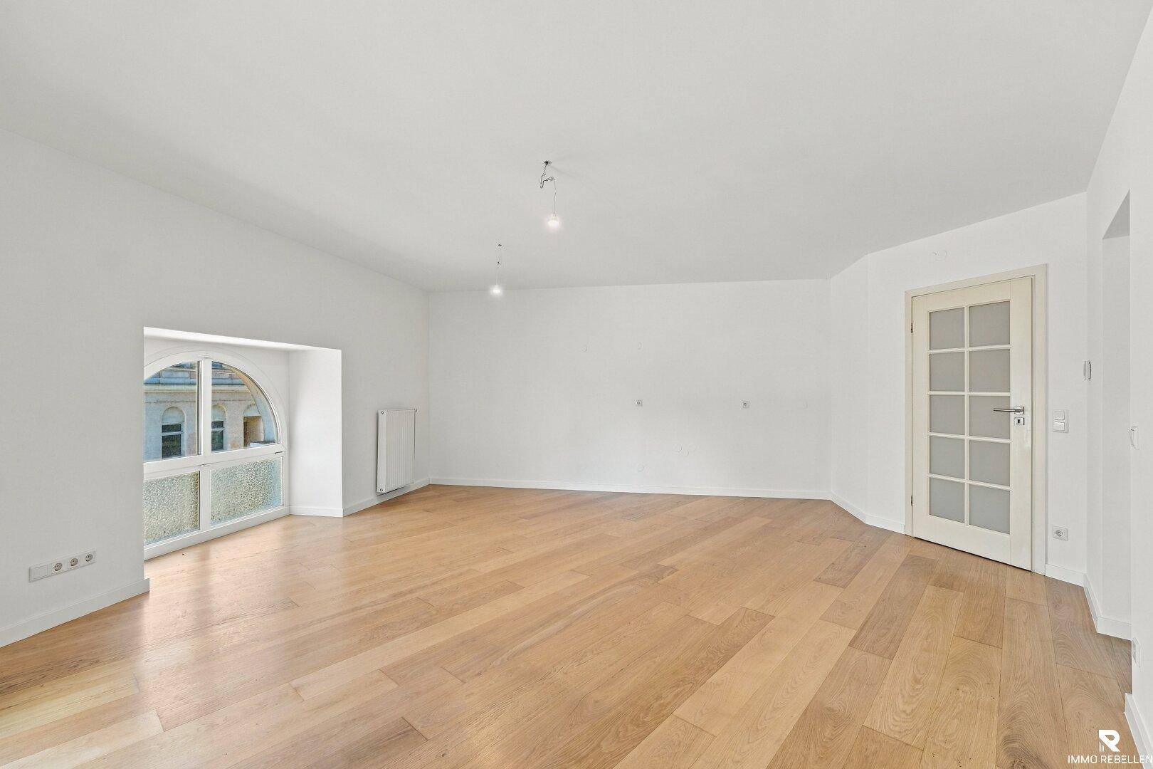 Geräumiges, leeres Zimmer mit Holzboden und einer Tür mit Glaseinsätzen, ideal für Wohnzwecke.