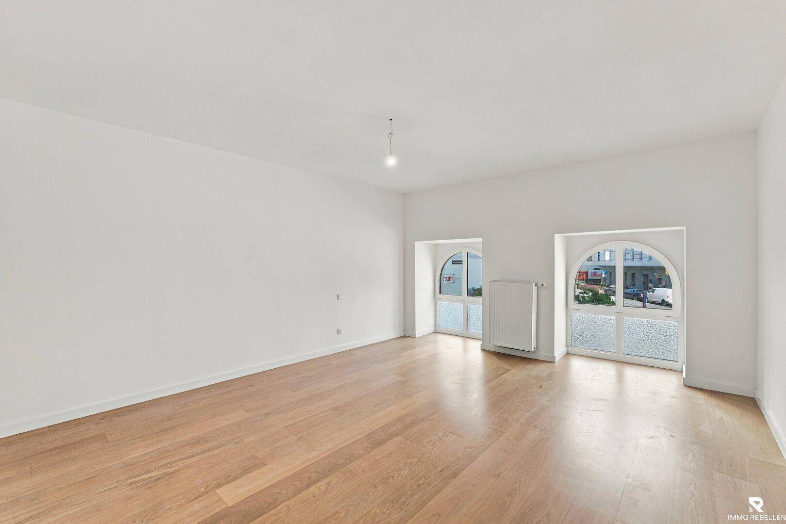 Leeres Schlafzimmer mit Holzboden und zwei großen Rundbogenfenstern, bietet viel Potenzial.