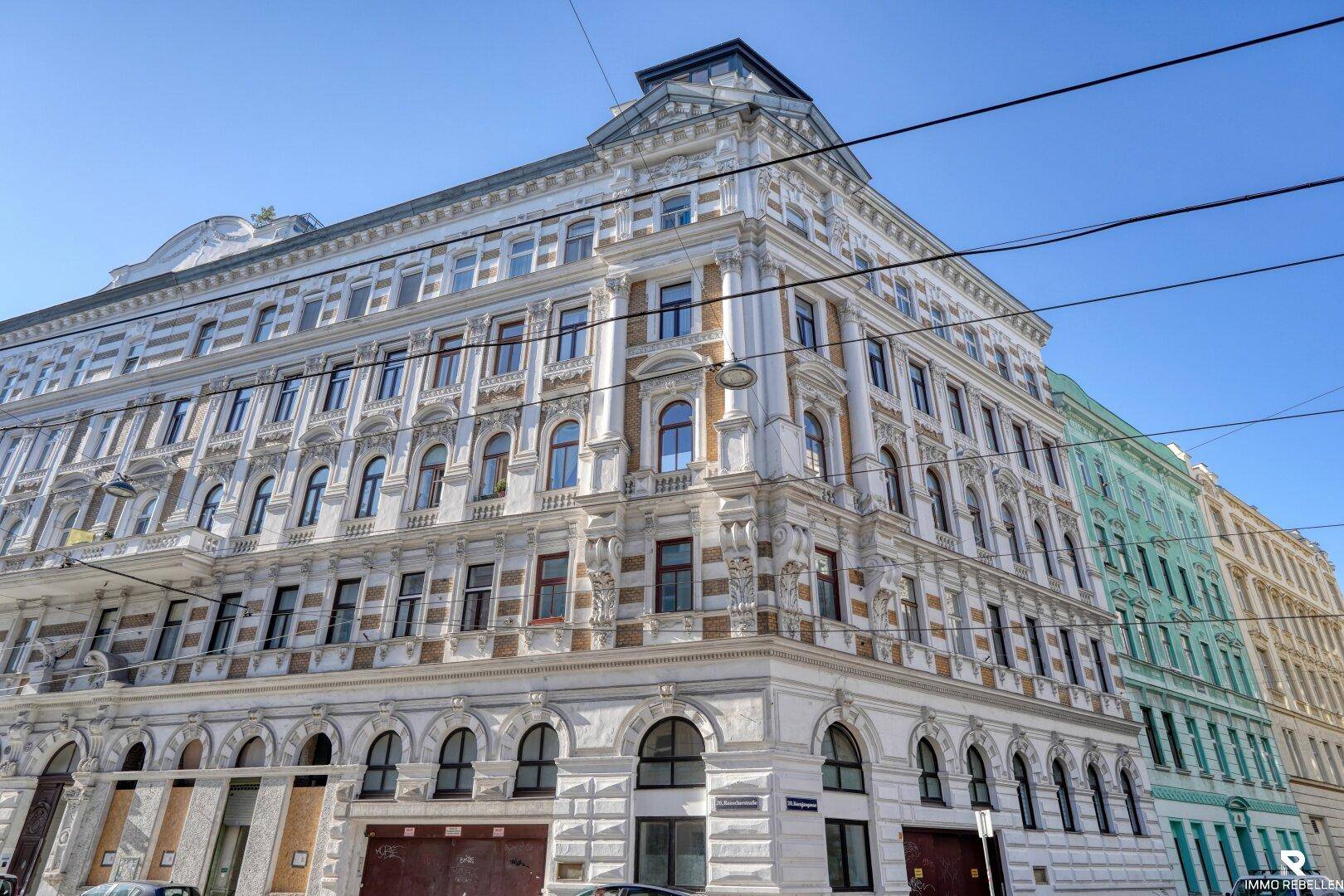 Prächtiges Eckgebäude mit reich verzierter Fassade und vielen Fenstern unter blauem Himmel.