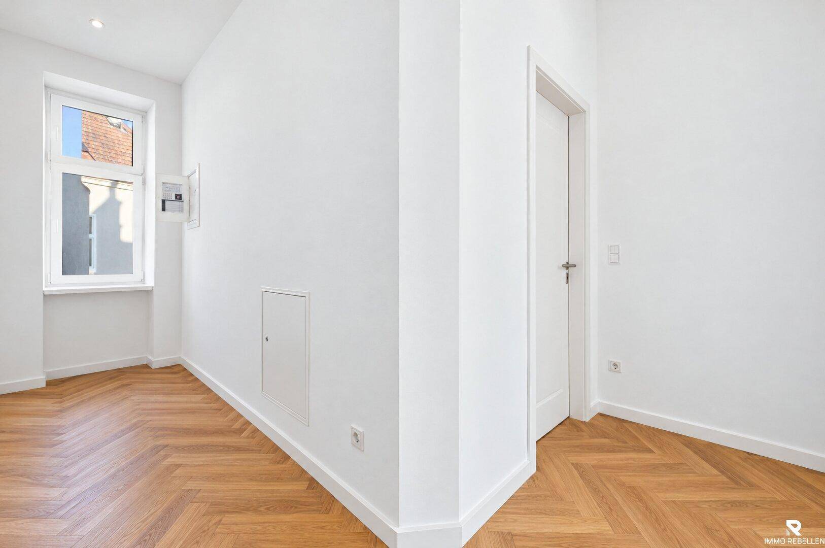 Heller Flur mit Fischgrätparkettboden und einem Fenster, das Tageslicht hereinlässt.