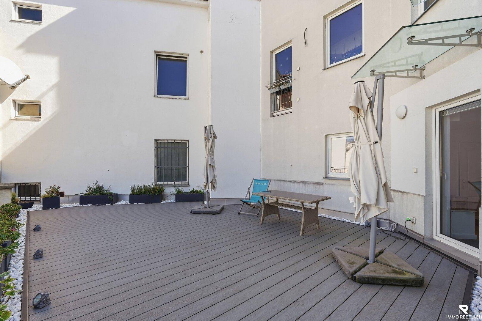 Weitläufige Terrasse mit Holzoptik-Bodenbelag und Blick auf die helle Gebäudefassade.
