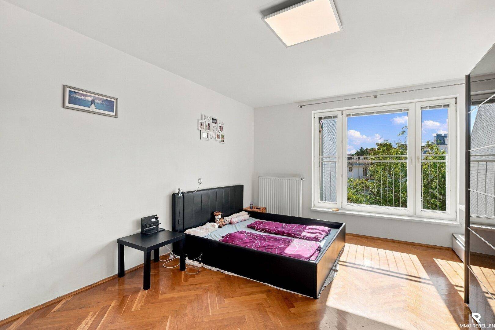Geräumiges Schlafzimmer mit Fischgrätparkett und großem Fenster, individuell eingerichtet.