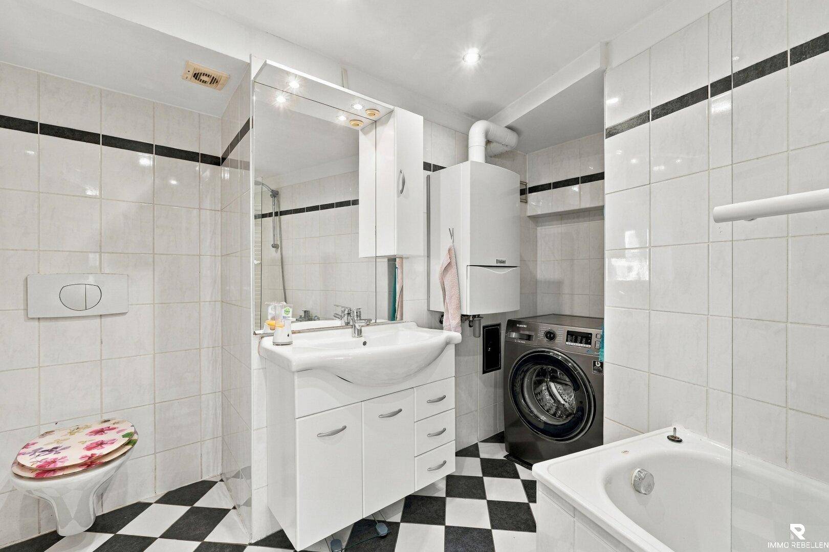 Badezimmer mit schwarz-weißem Fliesenboden, Badewanne, Waschbecken und Waschmaschine.