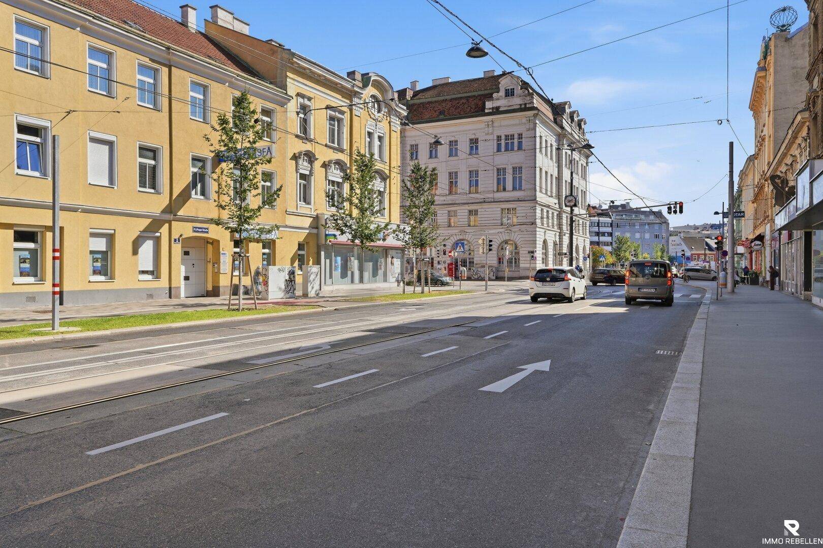 Belebte Stadtstraße mit historischen Gebäuden, Straßenbahnschienen und fahrenden Autos.
