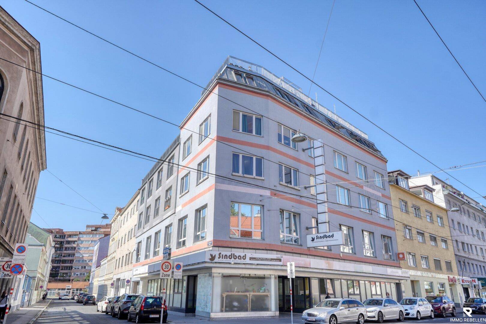 Gebäudefassade eines Mehrfamilienhauses an einer städtischen Straße mit Geschäften.